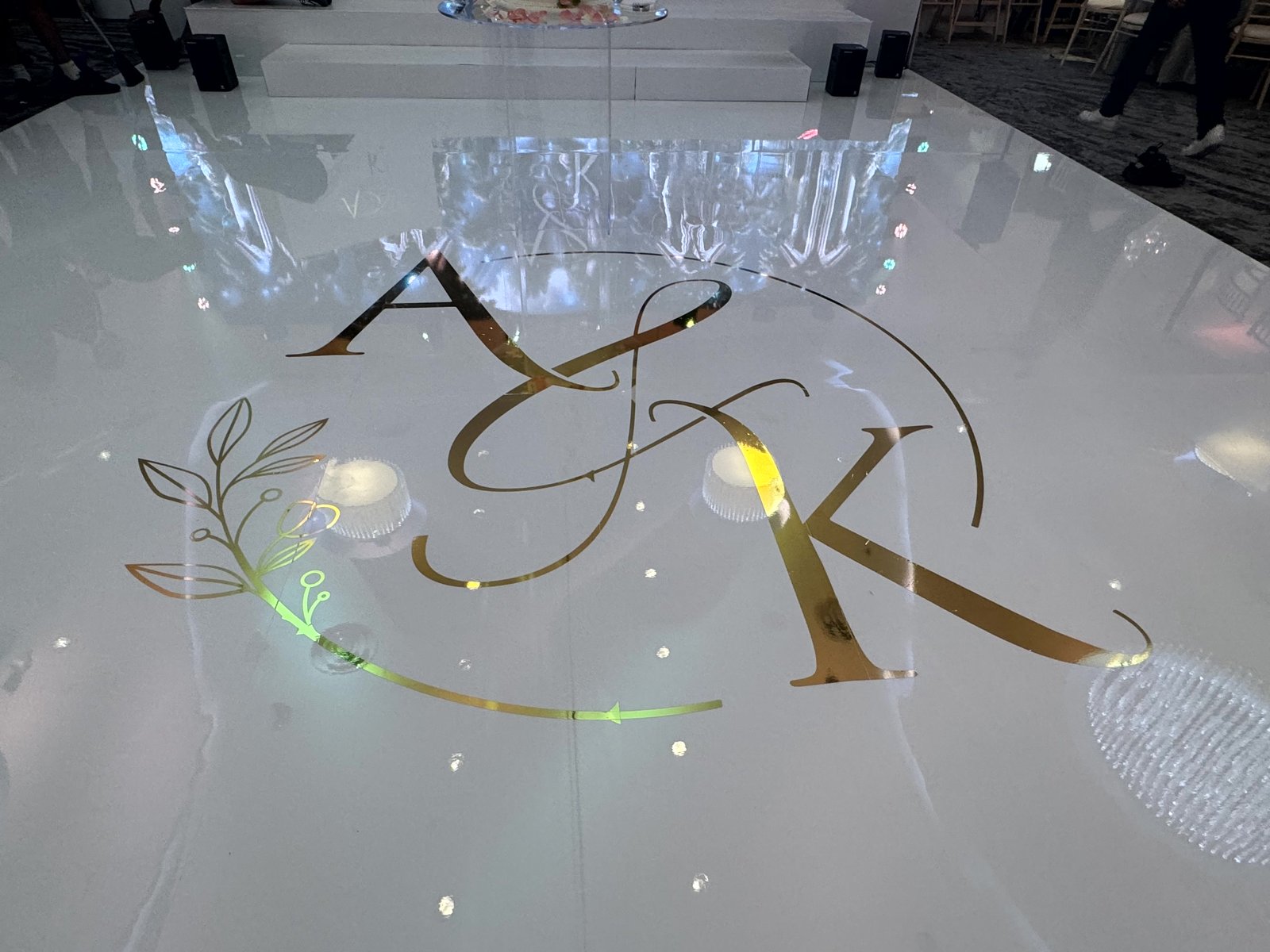 Elegant gold script monogram with floral flourish on a white seamless dancefloor